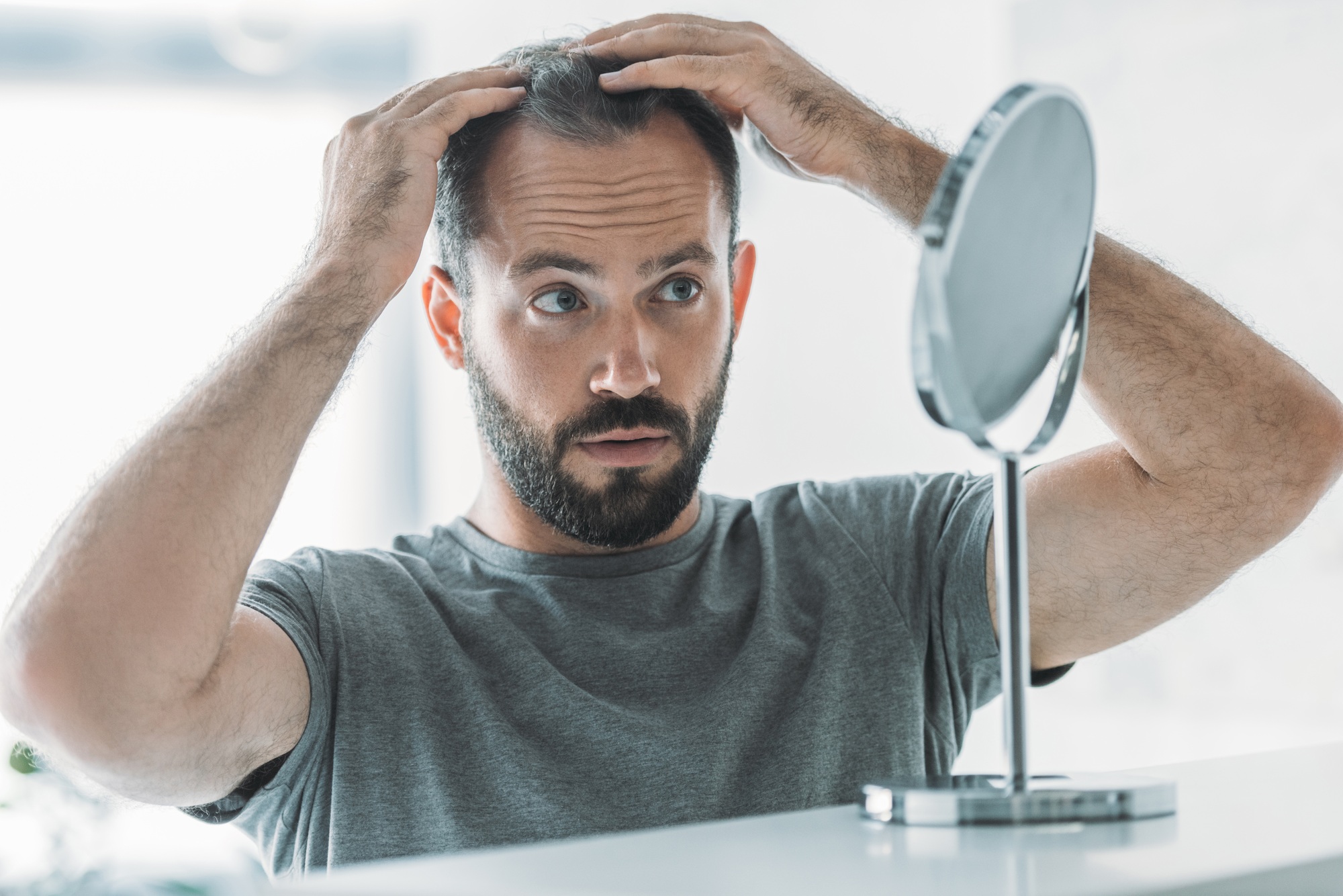 Man checking his hair loss in a handheld mirror