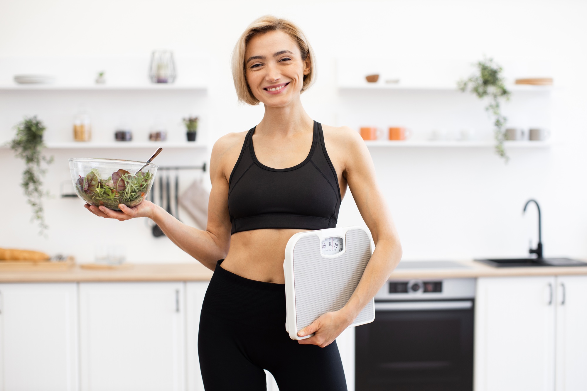 Woman with a fresh salad and scale in her kitchen, supporting healthy weight loss